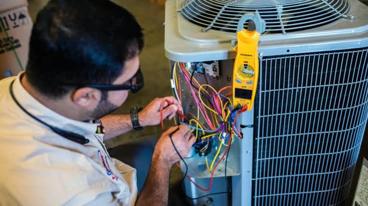 Technician testing electrical wiring on an outdoor air conditioning condenser
