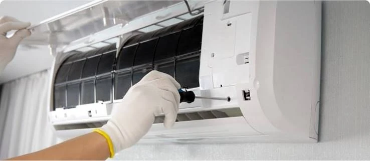 Gloved hands servicing the interior of a wall-mounted air conditioning unit